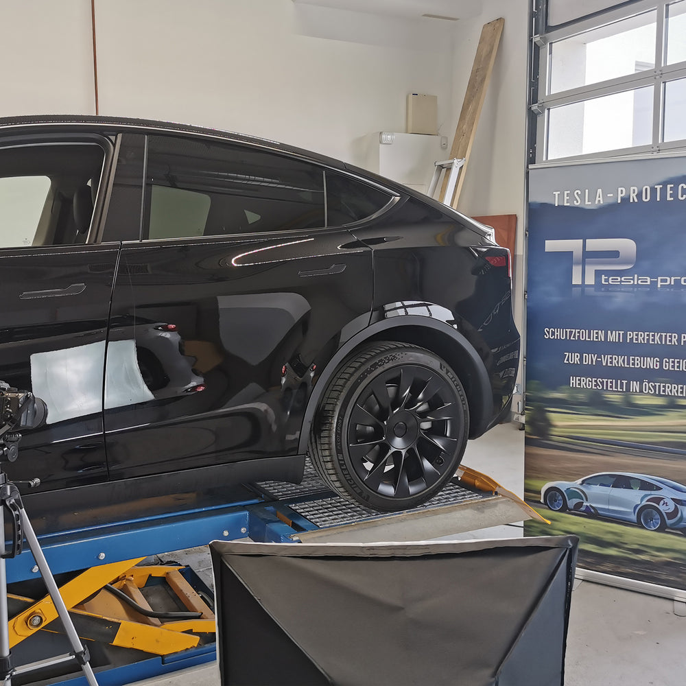 Sort Tesla Model Y på liften foran et banner fra Tesla-Protect